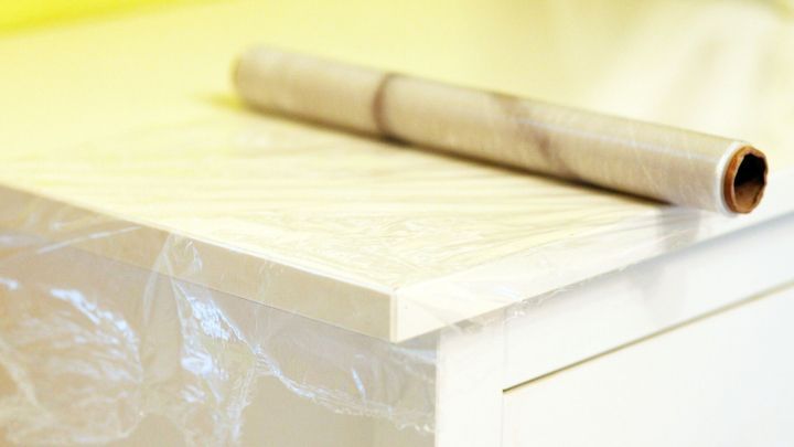 Eine Folie sch&uuml;tzt einen H&auml;ngeschrank vor Staub, w&auml;hrend eine Rolle transparentes Material daneben liegt.