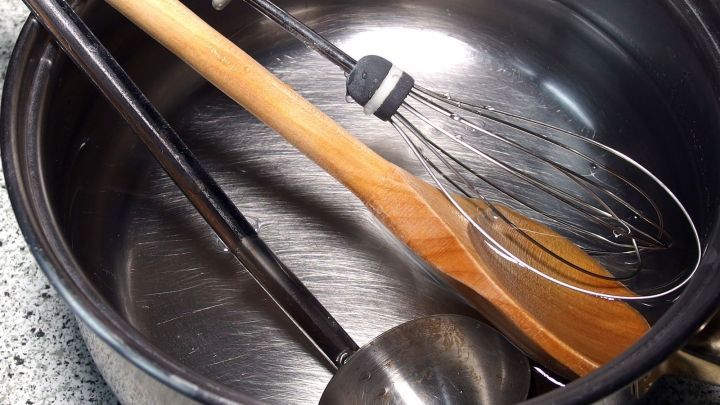 Ein L&ouml;ffeltopf mit lauwarmem Wasser enth&auml;lt Kochwerkzeuge wie einen Holzl&ouml;ffel, einen Schneebesen und einen Sch&ouml;pfl&ouml;ffel.