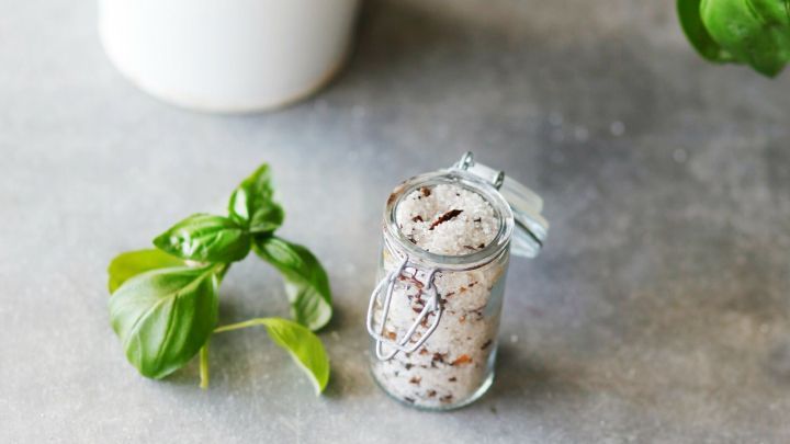 Ein Glas mit Kr&auml;utersalz steht neben einem Topf frischer Basilikumpflanze auf einer grauen Oberfl&auml;che.