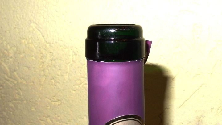 Eine Weinflasche ohne Korkenzieher wird ge&ouml;ffnet, steht an einer Wand mit heller Textur, der Deckel fehlt.