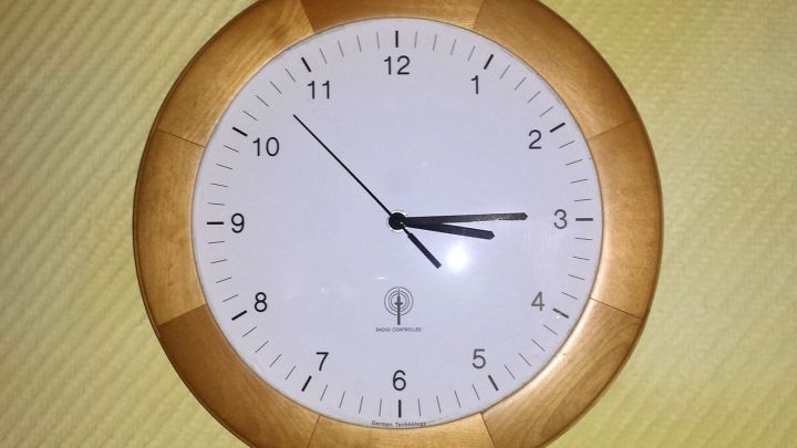 Holzuhr zeigt 10:10 an, h&auml;ngt an beige Wand. Text: "RADIO CONTROLLED German Technology".