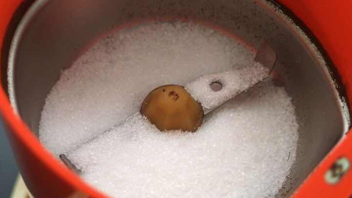 Eine Kaffeem&uuml;hle mit Schlagwerk enth&auml;lt wei&szlig;en Zucker und ein gemahlenes Material, w&auml;hrend sie zum Mahlen in Betrieb ist.