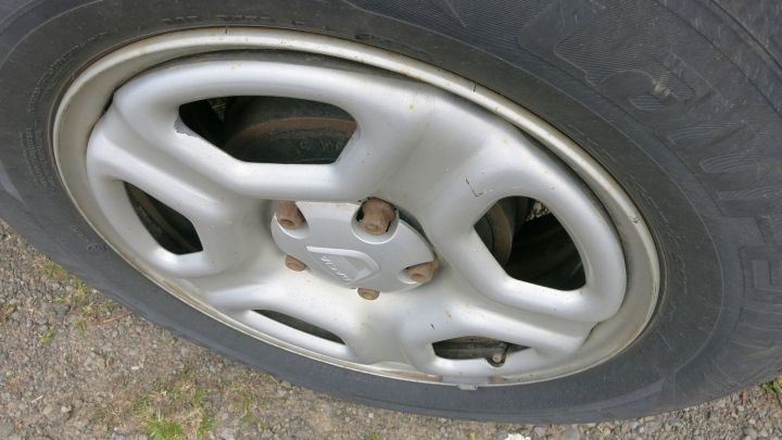 Die Felge eines Autos liegt auf dem Boden, w&auml;hrend sie sauber gewaschen wird. Wasser und Haarshampoo werden verwendet.