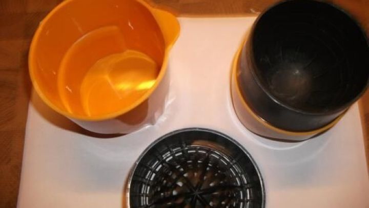 Orangenpresse zerlegt, zeigt orange und schwarze Teile auf Holzuntergrund, bereit zur Nutzung f&uuml;rs Auspressen.