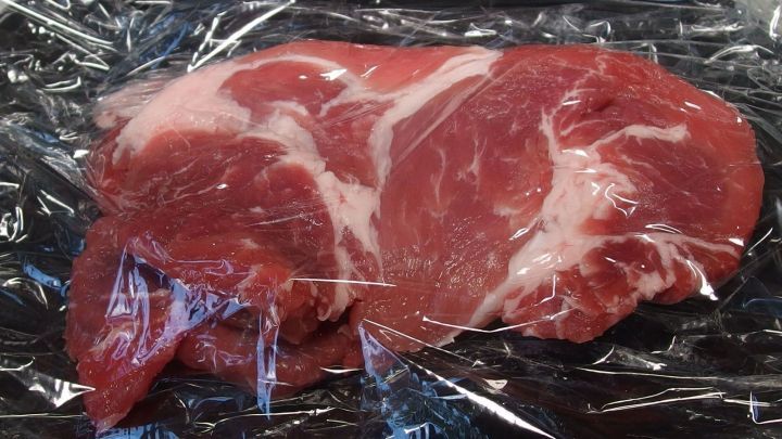 Zwei St&uuml;cke Schnitzel sind sorgf&auml;ltig in Frischhaltefolie eingewickelt und liegen auf einem dunklen Untergrund.