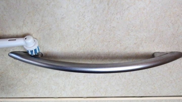 Eine alte Zahnb&uuml;rste wird zum Reinigen eines gl&auml;nzenden, gebogenen Handgriffs auf einer hellen Oberfl&auml;che verwendet.