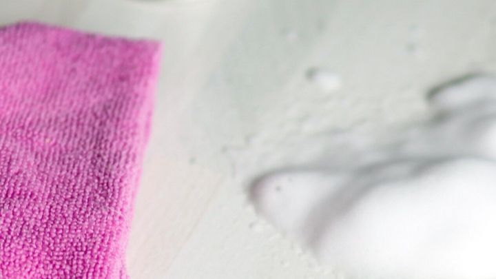 Ein pinkes Tuch liegt auf Laminat, daneben Schaum und eine Dose. Kontext: Reinigung von Laminat.