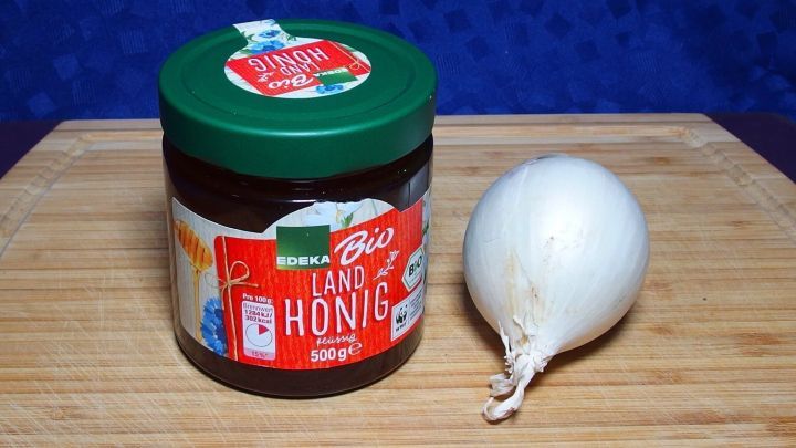 Ein Glas mit Zwiebel und Honig steht auf einem Holzbrett, um Erk&auml;ltungen und grippalen Infekt entgegenzuwirken.
