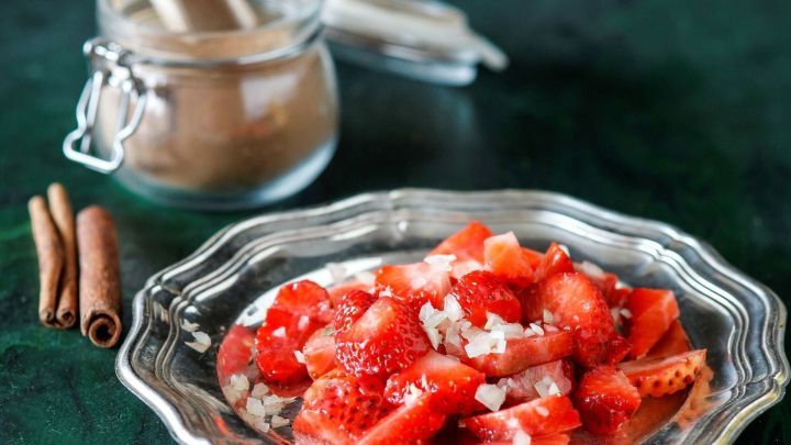Eine silberne Platte mit frischen Erdbeeren, die gew&uuml;rfelt und mit Zwiebeln garniert sind, steht auf einem gr&uuml;nen Tisch.