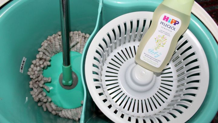 Ein Wischmopp steht in einem Eimer neben einer Flasche Baby&ouml;l, w&auml;hrend das Wasser zur Reinigung vorbereitet wird.