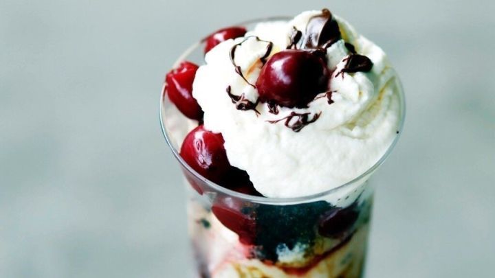 Ein Glas mit Pseudo Schwarzwaldbecher voller Schichten aus Sahne, Kirschen und Schokolade, serviert auf einem hellen Untergrund.