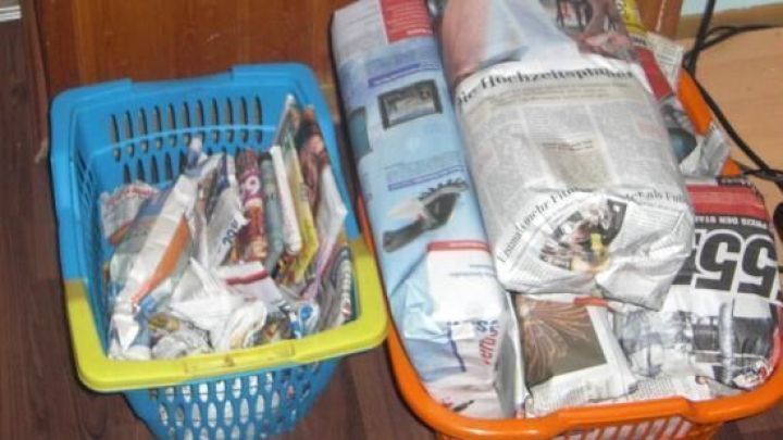 K&ouml;rbe gef&uuml;llt mit in Zeitungspapier eingepackten Geschenken stehen auf einem Holzboden vor einer Holzwand.