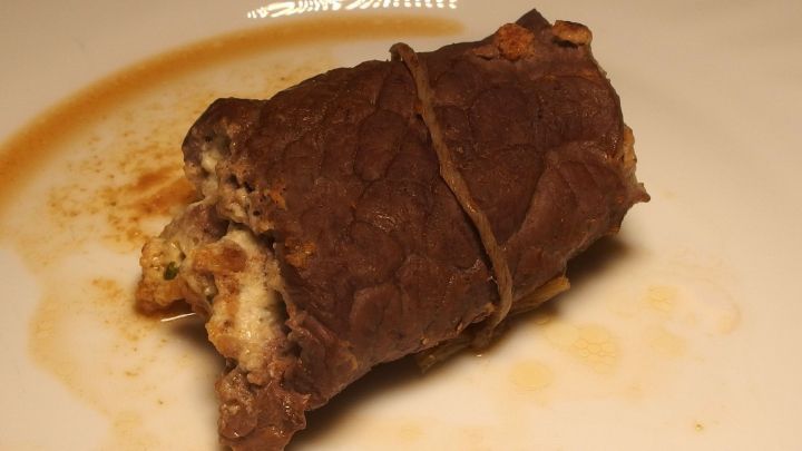 Ein Minutensteak wird kunstvoll gerollt und mit einer Schnur gebunden, serviert auf einem wei&szlig;en Teller mit Sauce.
