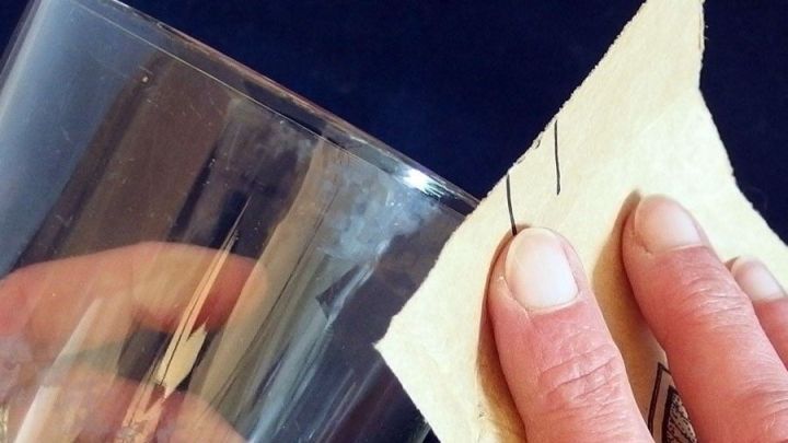Ein Glas wird mit Sandpapier bearbeitet, um einen kleinen Macken am Rand glatt zu schleifen.