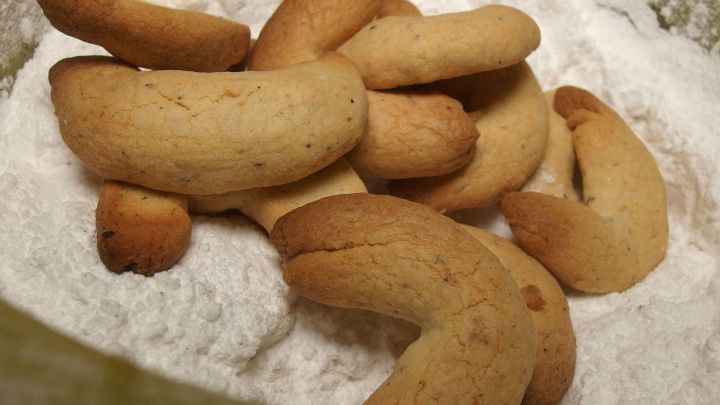 Zart gebackene Vanillekipferl liegen auf einem Haufen Puderzucker, bereit zum Zuckern in einer K&uuml;chenszene.