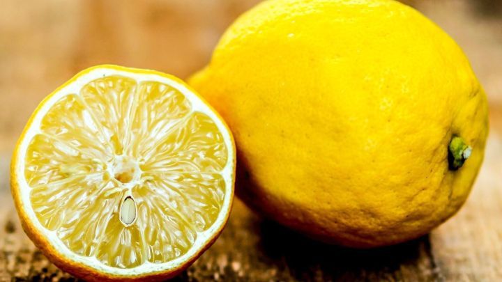 Eine gelbe Zitrone liegt neben einer halbierten Zitrone, die auf einem Holzbrett pr&auml;sentiert wird, ideal gegen Mundgeruch.