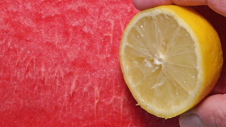 Eine halbierte Zitrone liegt auf einer Wassermelone, w&auml;hrend eine Hand sie h&auml;lt, um den erfrischenden Geschmack zu zeigen.