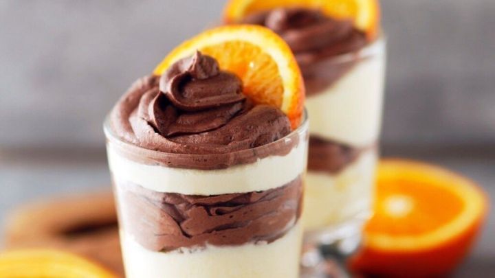 Zwei Schokoladendesserts in Gl&auml;sern auf einem Holzbrett, garniert mit Orangenscheiben, umgeben von frischen Orangen.