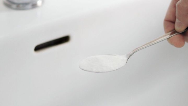 Ein L&ouml;ffel mit Soda wird &uuml;ber einem verstopften Waschbecken gehalten, um die Verstopfung zu l&ouml;sen.