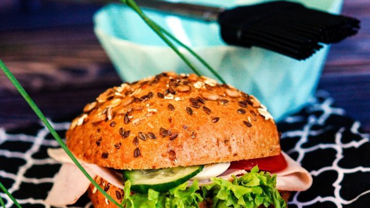 Ein frisch belegtes Butterbrot mit Salat, Gurke und Schinken liegt auf einem Tisch, w&auml;hrend ein Pinsel daneben steht.