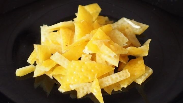 Streifen von Zitronenschalen liegen auf einem schwarzen Teller, bereit zur Verwendung in einem DIY-Raumduft-S&auml;ckchen.