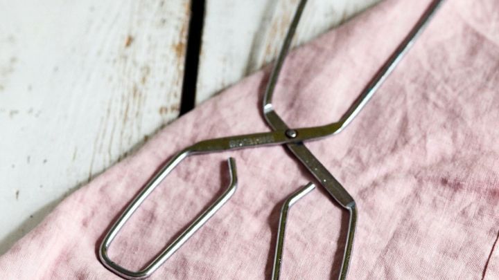 Eine Grillzange aus Metall liegt auf einem pinken Tuch und ist bereit, Speisen sicher und einfach zu greifen.