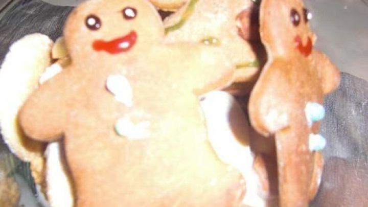 Lebkuchenm&auml;nnel liegen in einer Glassch&uuml;ssel, l&auml;chelnd und dekoriert, umgeben von mehr Lebkuchen und S&uuml;&szlig;igkeiten.