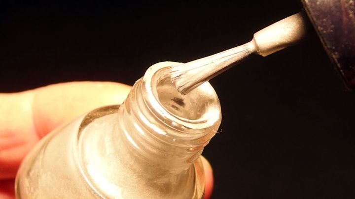 Ein Nagellackfl&auml;schchen wird ge&ouml;ffnet, w&auml;hrend ein Pinsel herausgezogen wird, bereit f&uuml;r das Auftragen gegen verf&auml;rbte Fugen.