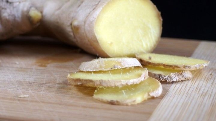 Frische Ingwerwurzel liegt auf einem Holzbrett, einige Scheiben sind geschnitten, bereit zum Kauen gegen Halsschmerzen.