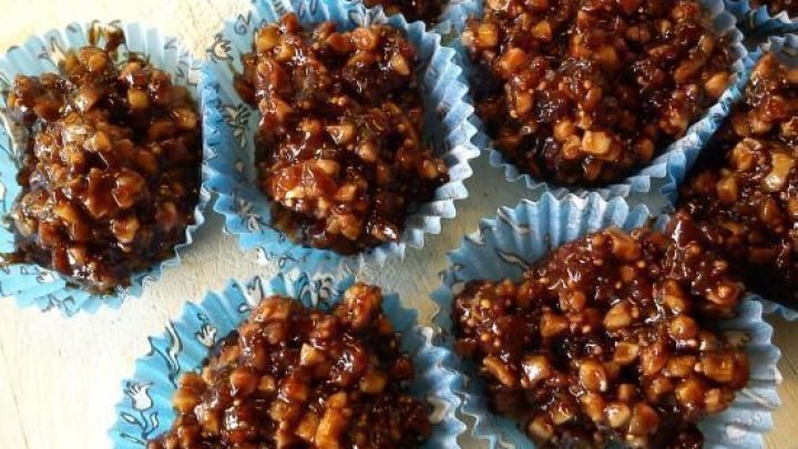 Kleine gesunde Leckerli aus N&uuml;ssen und Fr&uuml;chten in blauen F&ouml;rmchen auf einem Holzbrett, bereit zum Genie&szlig;en in der Adventszeit.
