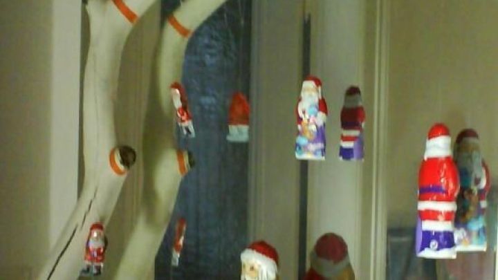 Ein wei&szlig;er Ast h&auml;ngt dekorativ von der Decke, geschm&uuml;ckt mit bunten Schokoladen-Weihnachtsm&auml;nnern in der Vorweihnachtszeit.