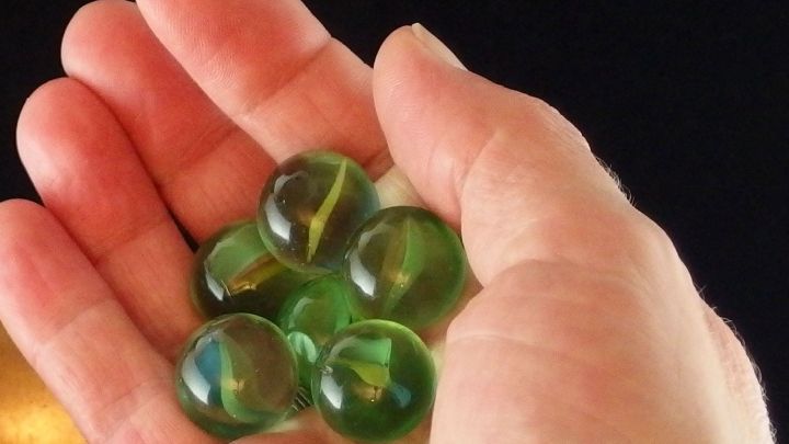 In einer Hand liegen mehrere gr&uuml;ne Murmeln, bereit f&uuml;r ein spannendes Murmelturnier bei schlechtem Wetter.