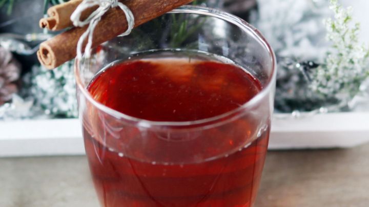 Ein Glas mit warmem Getr&auml;nk, verziert mit Zimtstangen, steht vor einer winterlichen Dekoration.