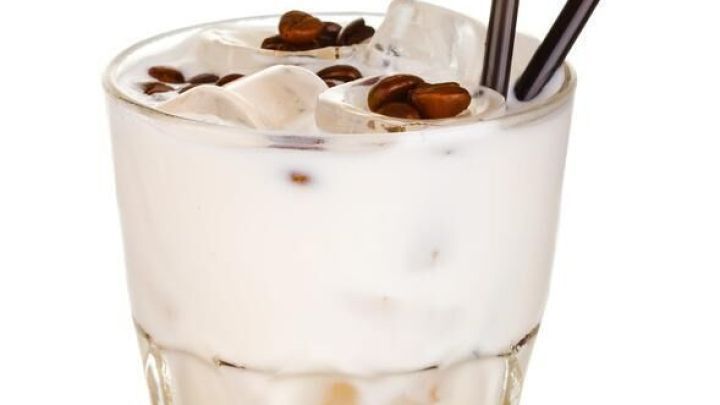 Ein Glas White Russian steht gef&uuml;llt mit Eisw&uuml;rfeln und Kaffeebohnen. Zwei Strohhalme ragen heraus, auf wei&szlig;em Hintergrund.