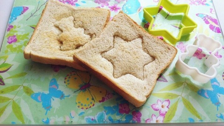 Auf einer bunten Unterlage liegen zwei Toastscheiben, die mit einer Ausstechform in Sternform verziert sind.