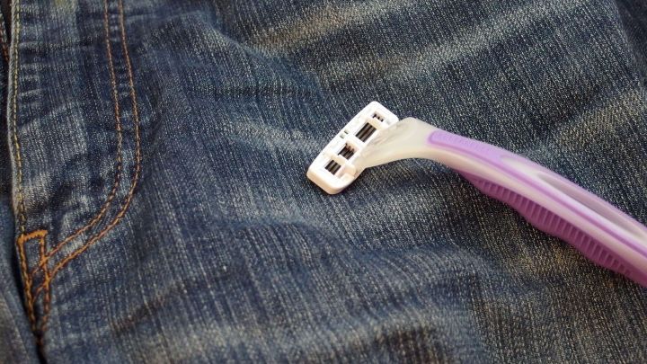 Eine Rasierklinge wird &uuml;ber den Stoff einer Jeans bewegt, um die Klingen zu sch&auml;rfen und ihre Lebensdauer zu verl&auml;ngern.