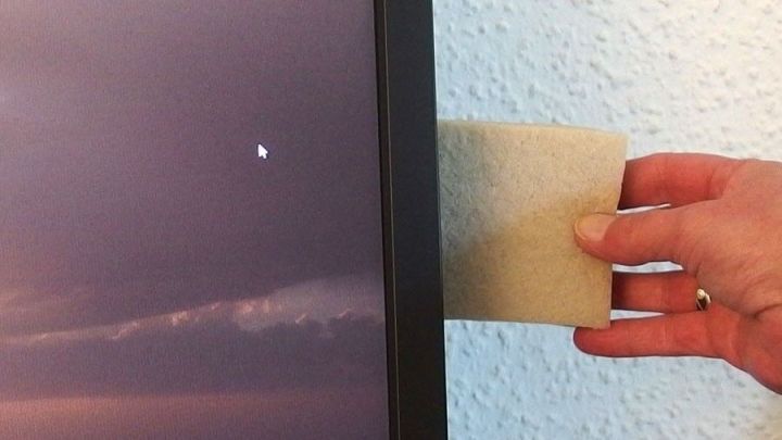 Ein Hand greift nach einem Schaumstoffst&uuml;ck, um ein schief h&auml;ngendes Bild an der Wand auszurichten.