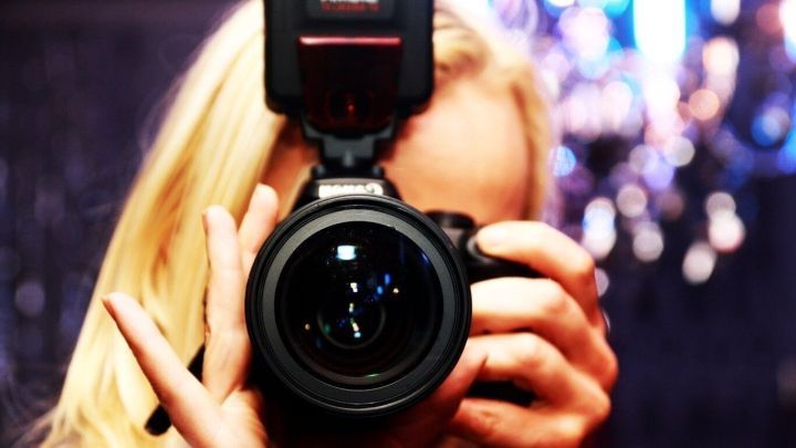 Eine Kamera wird von einer Person gehalten, die sich selbst fotografiert, umgeben von verschwommenen Lichtern.