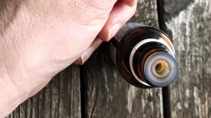 Eine hand h&auml;lt eine Flasche mit japanischem Minz&ouml;l, bereit zur Anwendung gegen verstopfte Nase auf einem Holztisch.