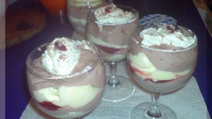 Dessertgl&auml;ser gef&uuml;llt mit Schwarzwaldcreme stehen auf einem Tisch. Die Creme ist geschichtet mit Sahne und Kirschkompott.