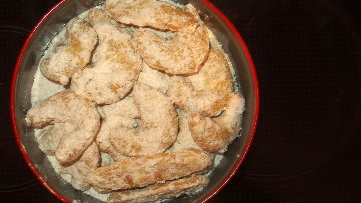 Dinkel-Vanillekipferl liegen gebacken in einer roten Sch&uuml;ssel und sind mit Puderzucker best&auml;ubt, bereit zum Servieren.