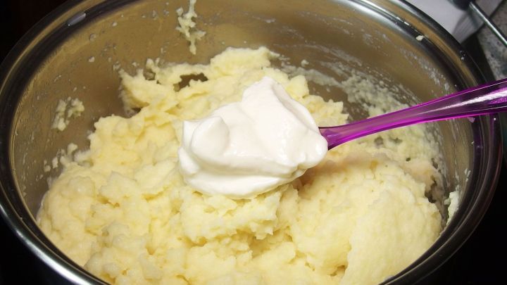 Eine Sch&uuml;ssel mit Kartoffelp&uuml;ree, in die ein L&ouml;ffel Frischk&auml;se gegeben wird, um es zu verfeinern.