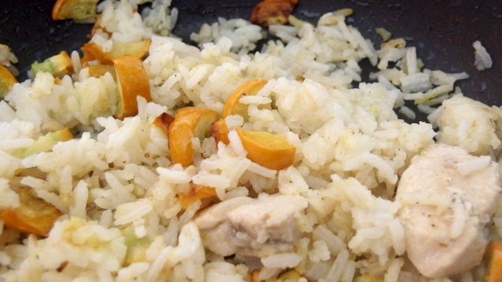 In einer Pfanne liegt gebratener Reis, der mit H&uuml;hnerst&uuml;ckchen und ger&ouml;steten Zutaten vermischt ist.