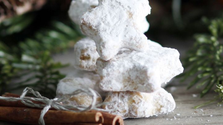 Zarte Nusskekse liegen &uuml;bereinander gestapelt, umgeben von gr&uuml;nem Tannenzweigen und einer Zimtschnecke im Hintergrund.