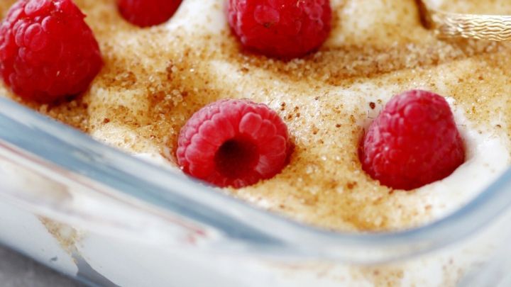 Ein Dessert aus Himbeerjoghurt und Sahne wird in einer Glasschale serviert, garniert mit frischen Himbeeren.