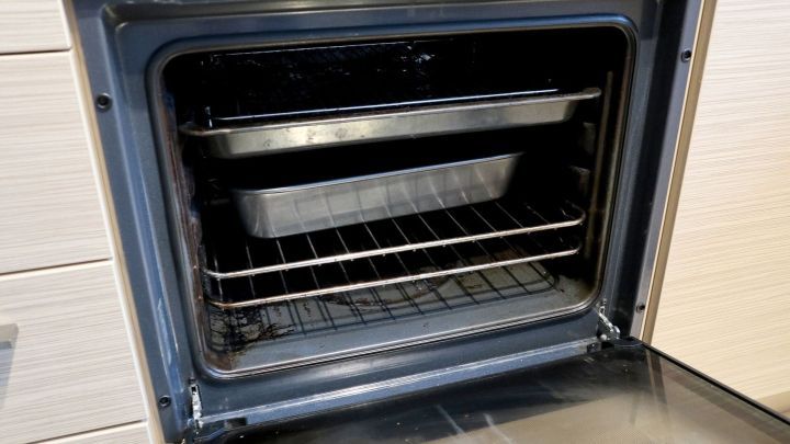 Ein ge&ouml;ffneter Backofen mit zwei leeren Backblechen auf den Rosten. Der schwarze Innenraum zeigt leichte Verunreinigungen.