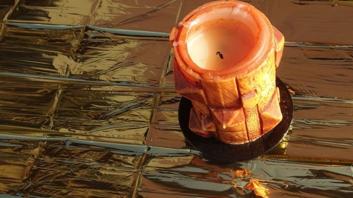 Eine Rettungsdecke liegt gl&auml;nzend auf dem Tisch, w&auml;hrend eine Kerze in einem Halter darauf brennt.