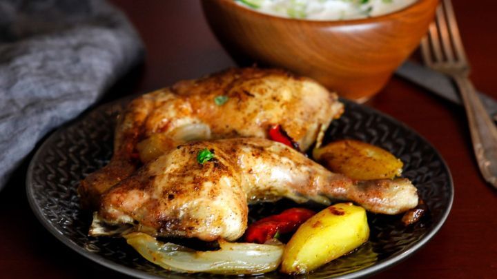 Zarte H&auml;hnchenschenkel liegen auf einem Teller mit gemischtem Gem&uuml;se, w&auml;hrend eine Sch&uuml;ssel Joghurt-Dip daneben steht.