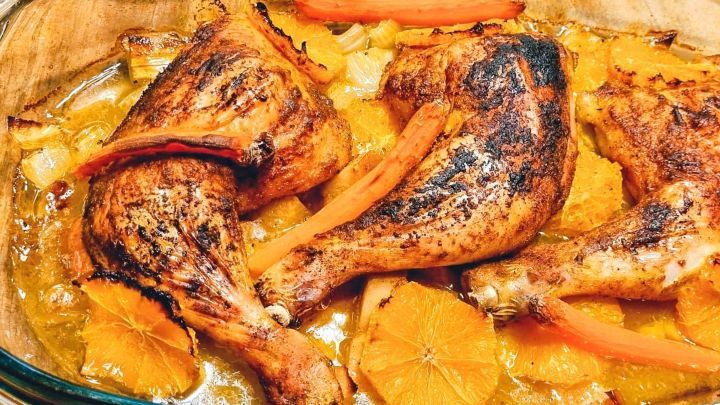 Saftige H&auml;hnchenschenkel liegen in einer Auflaufform, umgeben von Mandarinen und Gem&uuml;se, gebr&auml;unt und schmackhaft.