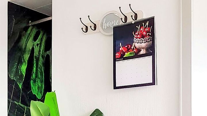 Ein Kalender h&auml;ngt an der Wand im Flur und zeigt ein fruchtiges Motiv, w&auml;hrend eine gro&szlig;e Pflanze daneben steht.